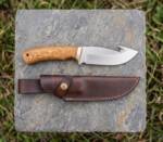 Harvest Moon D2 steel gut hook hunting knife with olive wood handle, brass bolster and brown leather sheath on stone