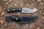 Redvein satin D2 gut hook hunting knife with black Micarta handle, red liners and black leather sheath on bare ground