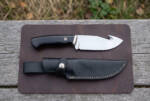 Midnight Horn satin D2 gut hook hunting knife with polished buffalo horn handle and black leather sheath on a leather mat
