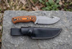 Blaze Hollow stonewashed D2 gut hook hunting knife with black and orange Micarta handle and black leather sheath on rock