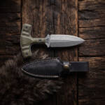 Trenchline stonewashed D2 push dagger with olive green Micarta T-handle and black leather sheath on dark wood