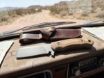 Dust Devil stonewashed D2 cowboy bull cutter knife with desert tan Micarta handle and leather sheath on a truck dashboard in the desert