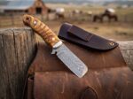 Plume Canyon feather Damascus cowboy bull cutter knife with ram horn handle, stainless bolster and leather sheath on a ranch fence