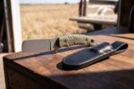 Olive Sidewinder stonewashed carbon steel cowboy bull cutter knife with sculpted olive green Micarta handle and black leather sheath on a barn workbench
