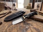Forge Shadow hand forged spring steel cowboy bull cutter knife with buffalo horn handle, brass bolsters and black leather sheath in a stable