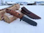 Ember Frost black oxide D2 cowboy bull cutter knife with black and orange Micarta handle and tooled leather sheath in the snow