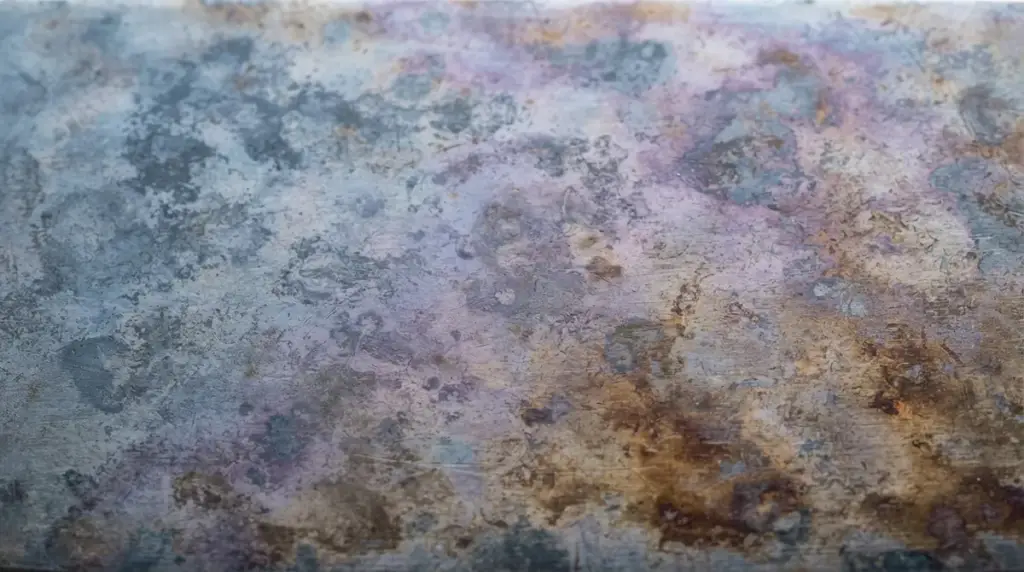 Macro of a carbon steel blade covered in a mottled blue grey and bronze patina
