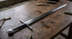 Ironcross D2 steel medieval European longsword with 36 inch mirror polished double edged blade, steel crossguard, black leather two handed grip and disc pommel on a workshop bench