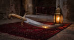 Desert Sultan handmade Damascus Arabian scimitar sword with high polish raindrop pattern curved blade, camel bone handle and hand engraved brass crossguard, lit by a brass lantern on a Persian rug