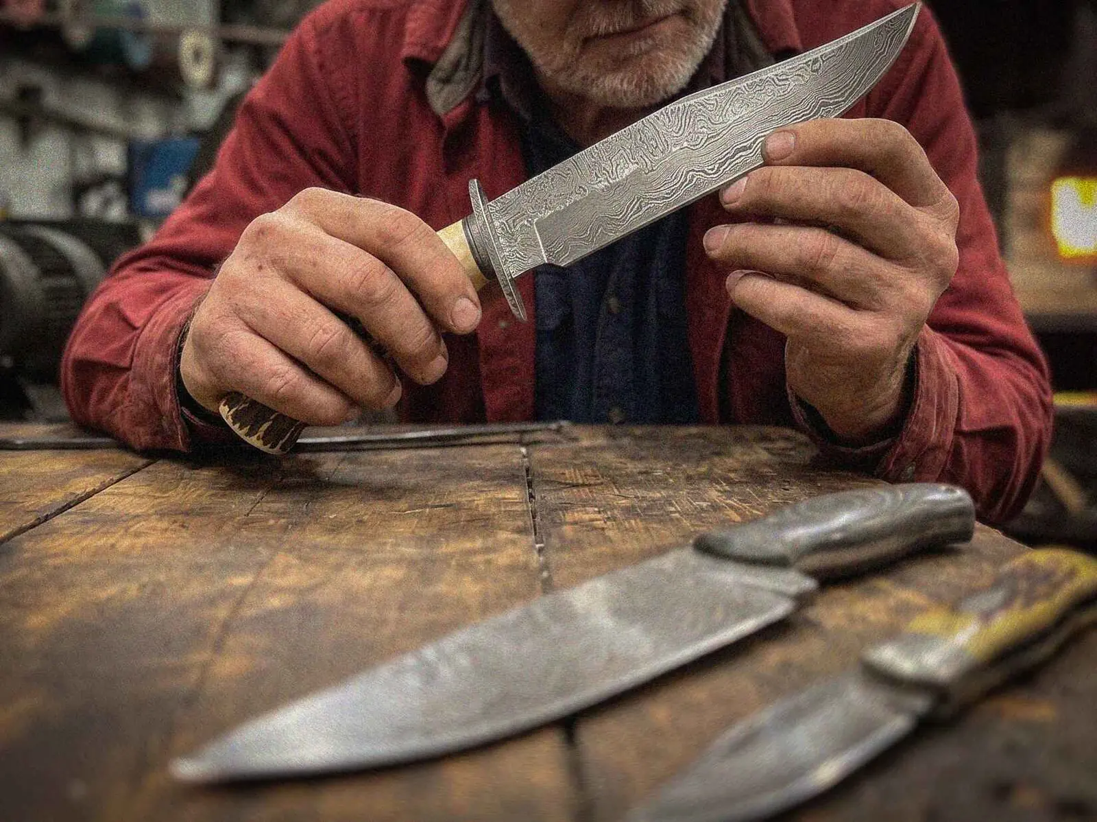 Mark Kovalsky inspecting a finished hand-forged Damascus bowie knife in the workshop