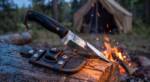 Crimson Vein mirror polished D2 steel bushcraft knife with smooth black G10 handle, red fibre spacer and mosaic pin at a woodland camp