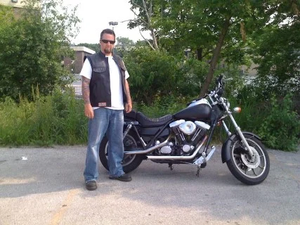 Virgil Shovelhead, bladesmith at Black Mamba Knives, standing beside his Harley